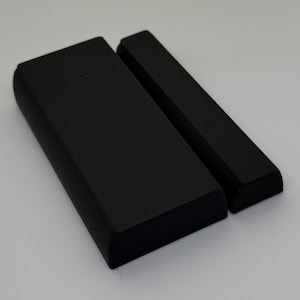 May include: Two matte black rectangular components with rounded edges. The larger piece is wide and flat, while the smaller piece is narrow and elongated. Both items feature a smooth, solid black finish and a uniform, geometric design.