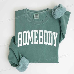 May include: A light green sweatshirt with the word "HOMEBODY" printed in white on the front.