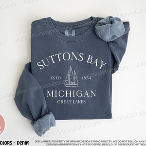 May include: A dark blue sweatshirt with a white graphic design that says "Suttons Bay Est. 1854 Michigan Great Lakes" with a sailboat illustration.