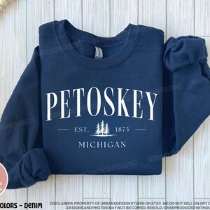 May include: A navy blue sweatshirt with white text that reads "Petoskey Est. 1873 Michigan" with a small graphic of pine trees.