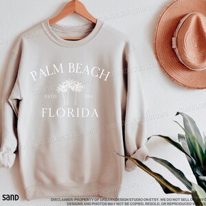 May include: A sand-colored sweatshirt with a white graphic design that says "Palm Beach Florida" with palm trees and the text "Est. 1911".
