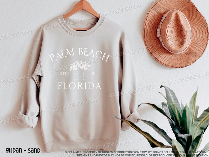 May include: A sand-colored sweatshirt with a white graphic design that says "Palm Beach Florida" with palm trees and the text "Est. 1911".