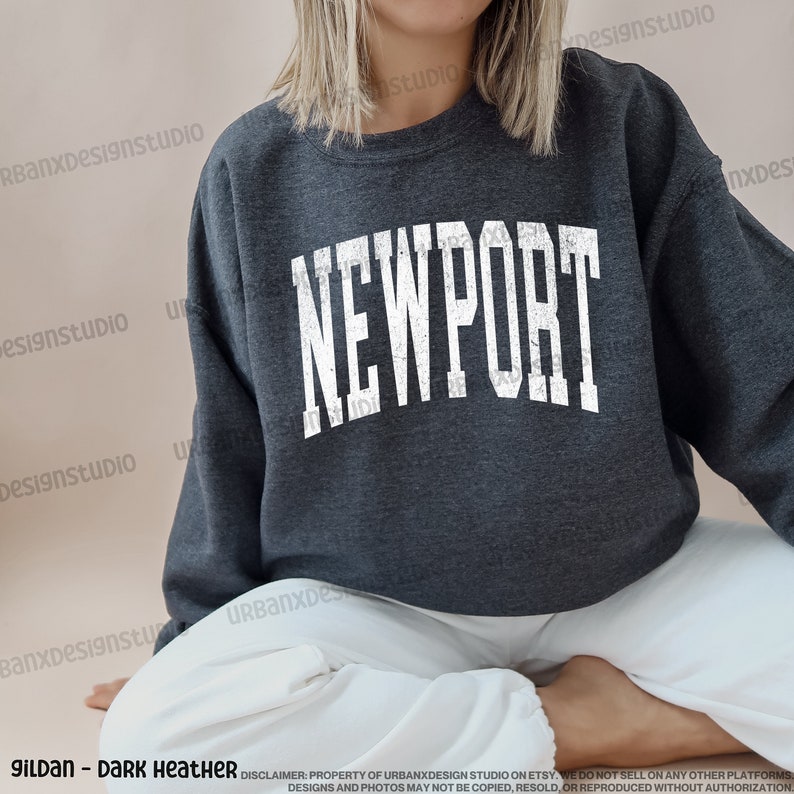 May include: A dark heather grey sweatshirt with the word "NEWPORT" printed in white on the front. The sweatshirt has a distressed, vintage look.
