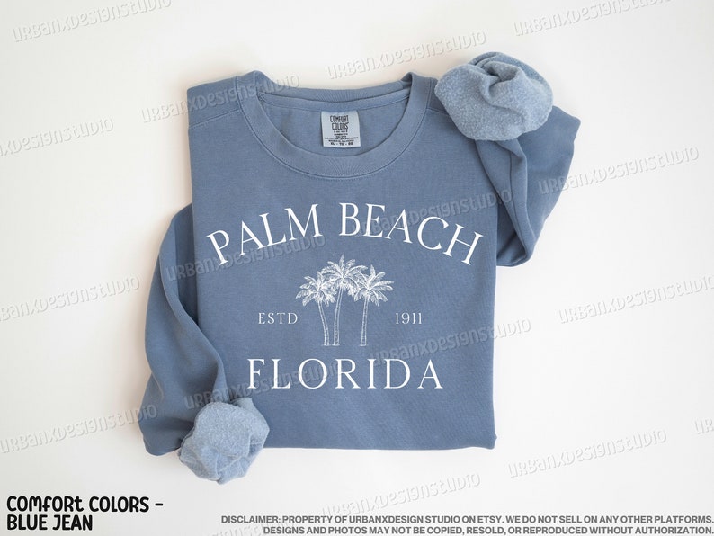 May include: A blue jean sweatshirt with white text that reads "PALM BEACH ESTD 1911 FLORIDA" and a graphic of palm trees.