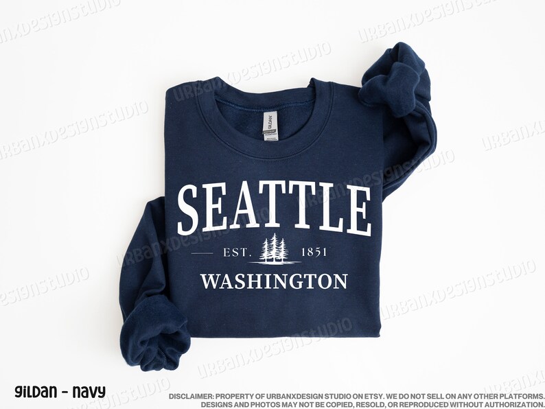 May include: A navy blue sweatshirt with white text that reads "SEATTLE - EST. 1851 - WASHINGTON" with a graphic of pine trees.