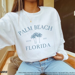 May include: White sweatshirt with a blue graphic print of palm trees and the text "Palm Beach, Estd 1911, Florida".