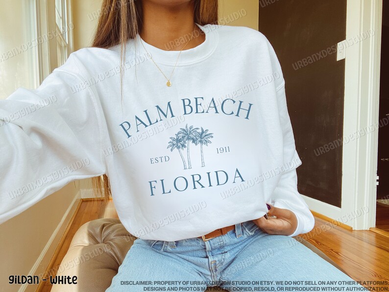 May include: White sweatshirt with a blue graphic print of palm trees and the text "Palm Beach, Estd 1911, Florida".