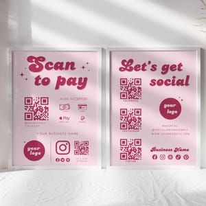 May include: Two framed pink posters with white borders. One says "Scan to pay" and the other says "Let's get social." Both have QR codes and social media icons. A white vase with dried plants sits to the right.