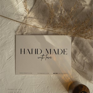 May include: A white card with the text "HAND MADE with love" in black lettering. Below the text are the words "WWW.WEBSITE.COM YOUR@EMAIL.COM @SOCIALHANDLE". The card is on a beige surface with a dried grass sprig and a brown glass bottle.