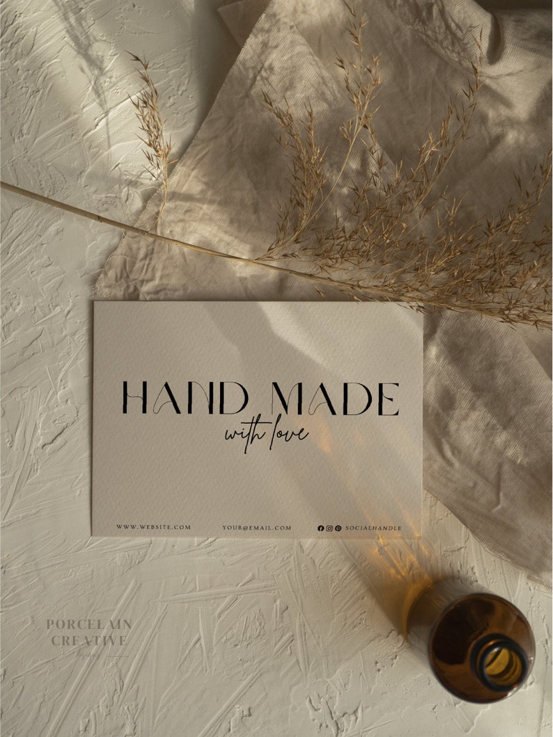 May include: A white card with the text "HAND MADE with love" in black lettering. Below the text are the words "WWW.WEBSITE.COM YOUR@EMAIL.COM @SOCIALHANDLE". The card is on a beige surface with a dried grass sprig and a brown glass bottle.