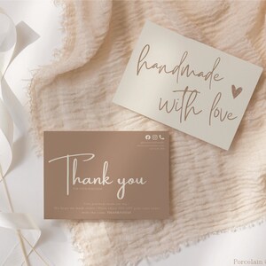 May include: Two cards with handwritten text on a beige fabric background. The top card is beige and says "handmade with love" with a small heart icon. The bottom card is brown and says "Thank you" with additional text about the product being handmade with love.