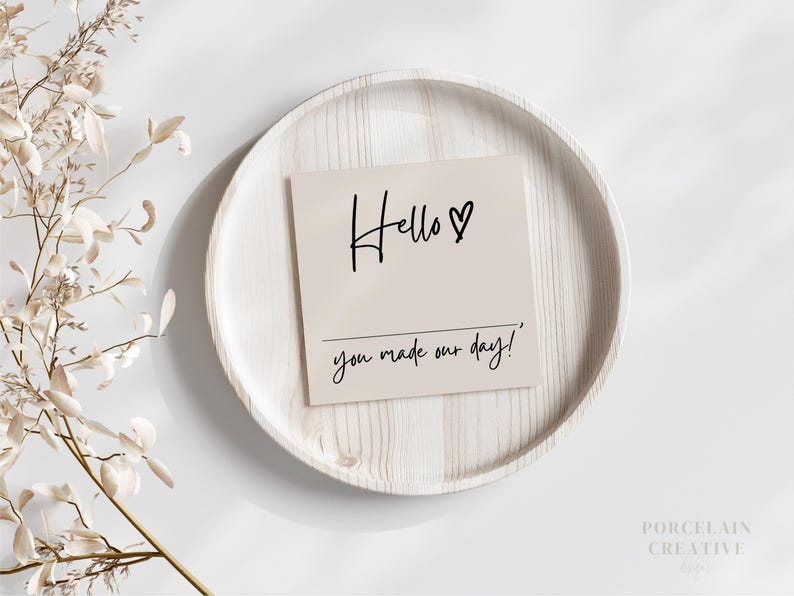 Op de afbeelding: Een witte kaart met zwarte kalligrafie met de tekst "Hello &hearts; you made our day!" De kaart ligt op een wit houten bord.