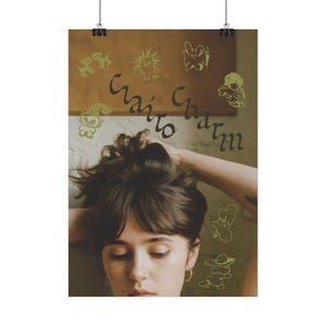 Peut inclure: Une affiche avec l'inscription "Waits Charm" dans une police manuscrite et plusieurs illustrations de dessins animés en vert clair. L'affiche représente une personne aux cheveux foncés, portant des créoles dorées et un piercing au nez.