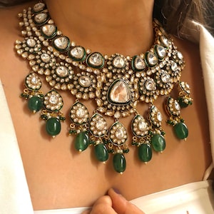 May include: A gold and green statement necklace with large, clear gemstones and emerald green beads. The necklace has a layered design with multiple tiers of stones and beads.
