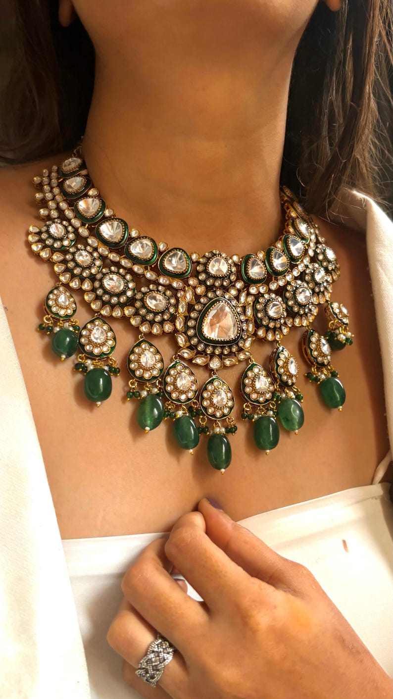 May include: A gold and green statement necklace with large, clear gemstones and emerald green beads. The necklace has a layered design with multiple tiers of stones and beads.