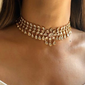 May include: A gold choker necklace with a floral design featuring white and red gemstones. The necklace is made of metal and has a delicate, intricate design.