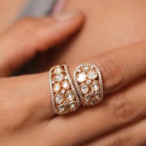 Peut inclure: Une bague en or au design unique avec une double bande sertie de nombreux petits diamants ronds et en forme de poire.