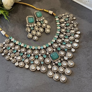 May include: A silver and green statement necklace with a large emerald green stone in the centre. The necklace is adorned with smaller emerald green stones and clear rhinestones. Matching earrings with a smaller emerald green stone are also included.