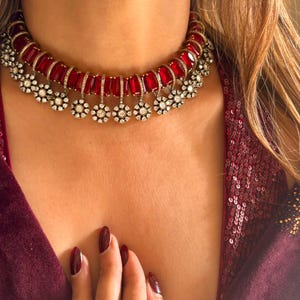 May include: A red and silver choker necklace with a row of red stones and dangling silver flower-shaped charms.