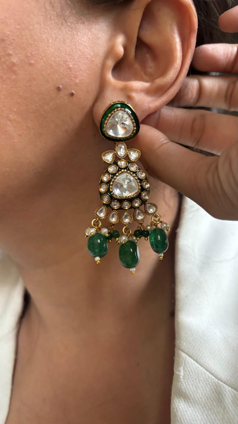 May include: Gold earrings with a large, clear, faceted gemstone surrounded by smaller gemstones. The earrings have a green enamel base and dangle with green and white beads.