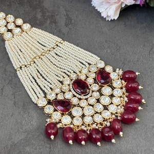 Peut inclure: Un collier doré orné d'un groupe central de pierres rouges et de cristaux transparents. Le collier est composé de brins de petites perles blanches et de perles rouges en forme de goutte. Le design est complexe et détaillé, idéal pour les occasions spéciales.