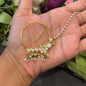 May include: A gold nose ring with a chain and a cluster of white and green stones.