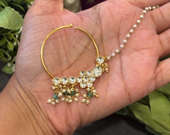 May include: A gold nose ring with a chain and a cluster of white and green stones.