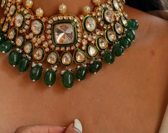 May include: A gold and green statement necklace with large, faceted gemstones and emerald green beads. The necklace is adorned with small pearls and intricate details.