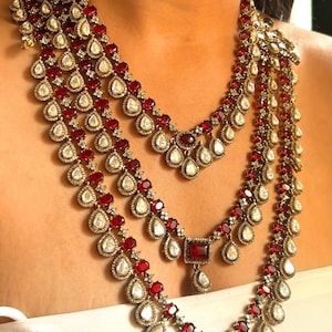 May include: A multi-strand necklace with a teardrop-shaped pendant. The necklace is made of gold and features red and white gemstones.