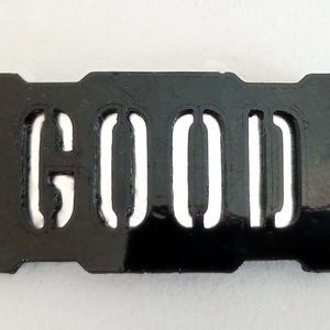May include: A black plastic sign with the word "GOOD" cut out in white.