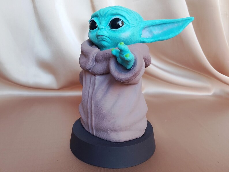 K&ouml;nnte beinhalten: Eine kleine, blaue und gr&uuml;ne Figur eines Charakters aus dem Star Wars-Franchise, die eine braune Robe tr&auml;gt. Die Figur steht auf einem schwarzen Sockel.