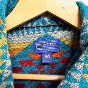 May include: A Pendleton brand garment featuring a vibrant geometric pattern in shades of turquoise, yellow, orange, and red. A blue rectangular label is stitched at the collar, reading: WARRANTED TO BE A PENDLETON, PENDLETON WOOLEN MILLS, SINCE 1863, ONE SIZE, MADE IN EL SALVADOR OF USA FABRIC.