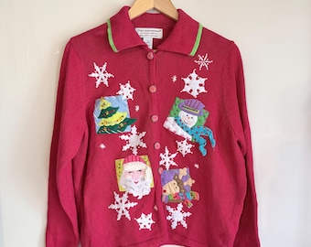 May include: A red Christmas cardigan sweater with a collared neckline and button-up front. The sweater features appliqued holiday designs, including a Christmas tree, snowman, Santa Claus, and a reindeer. White snowflake accents are scattered across the front.