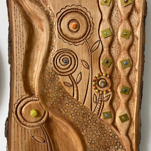 May include: Wooden wall art with carved floral and abstract designs. The artwork features a natural wood tone with intricate details, including carved flowers, spiral patterns, and embedded beads. The piece has a rustic, handcrafted aesthetic.