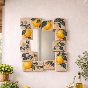 May include: Square mirror framed with decorative tiles featuring yellow lemons and white flowers on a beige background. The mirror is surrounded by a wooden table with a bowl of lemons, plants, and decorative items.