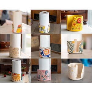 May include: A collection of decorative paper towel holders. Each holder features a unique design, including floral, fruit, and geometric patterns. The holders are made of ceramic and are designed to hold a standard paper towel roll. The colors include yellow, blue, pink, and white.