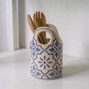 Op de afbeelding: Set van drie keramische mokken met een gespikkelde, crèmekleurige glazuur. Elke mok heeft een handgeschilderd bloemmotief in blauw, groen en geel. De mokken hebben een eenvoudige, afgeronde vorm en een handvat.