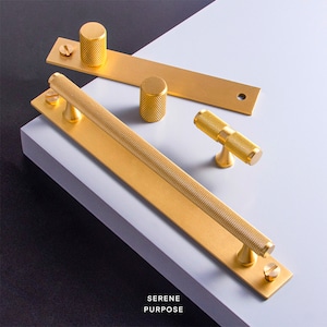 May include: A set of five gold-toned cabinet hardware pieces, including a long bar pull, a small knob, a t-shaped pull, and two smaller knobs. The hardware has a textured, slightly rough surface.