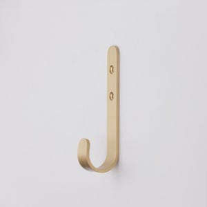 May include: A gold-toned metal hook with a curved design. The hook is mounted on a white wall.