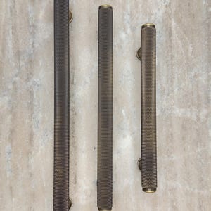 May include: Three different sizes of antique brass door pulls with a textured, diamond-shaped pattern.