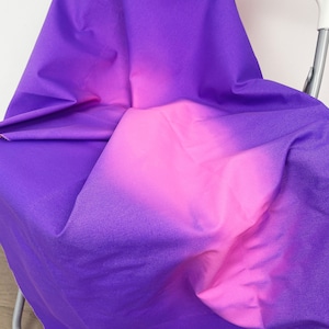 May include: A purple and pink ombre fabric with a soft, smooth texture. The fabric is folded and draped over a chair.