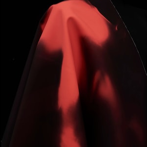May include: A close-up of a red fabric draped over a black surface. The fabric is smooth and shiny, with a slight sheen.