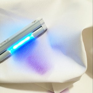 May include: A white fabric with a purple stain being illuminated by a handheld UV light.