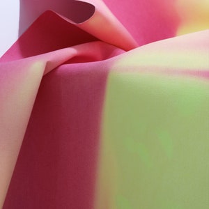 以下が含まれることがあります： ピンク、イエロー、グリーンのグラデーションパターンが施されたファブリックのクローズアップ。ファブリックは折り畳まれており、柔らかく質感のある表面をしています。