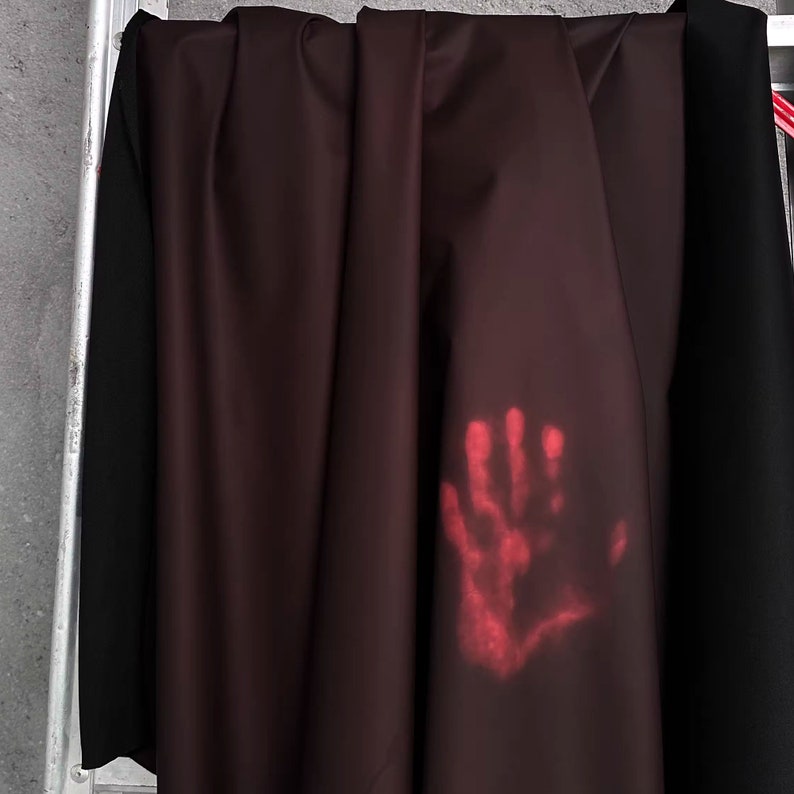 May include: A close-up of a dark red fabric with a faint red handprint on it. The fabric is hanging on a metal ladder.