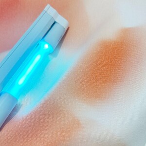 Puede incluir: Un desinfectante UV azul claro, de forma rectangular, que emite un brillo azul brillante. Descansa sobre una tela blanca y color melocotón.