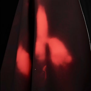 May include: A close-up of a dark red fabric with a red light shining through it, creating a blurry, abstract pattern.