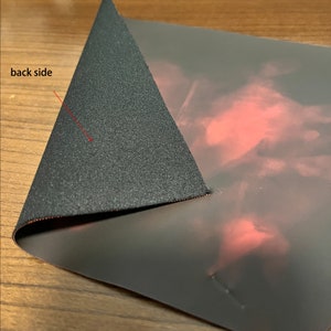 May include: A black mouse pad with a red and pink design on the front. The back side of the mouse pad is black.