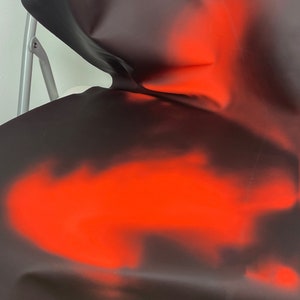 May include: A black fabric with a red ombre effect. The fabric is draped over a chair.