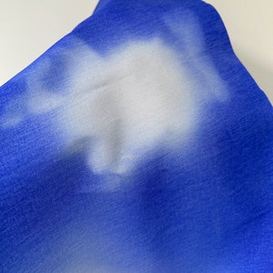 May include: Close-up of a blue denim fabric with a white bleached design. The fabric has a soft, textured feel.
